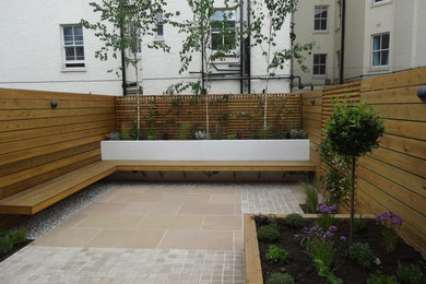 Small contemporary back full sun garden for summer in London with natural stone paving.