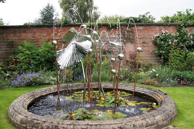 Imagen de jardín clásico grande en verano en patio trasero con jardín francés, fuente y exposición total al sol