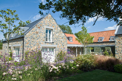 This is an example of a large farmhouse back full sun garden for summer in Channel Islands with natural stone paving.
