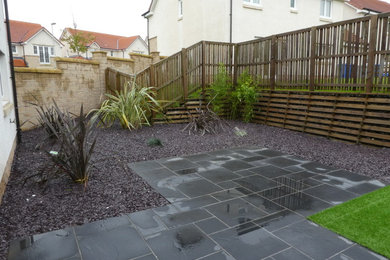 This is an example of a contemporary back formal garden in Glasgow with natural stone paving.
