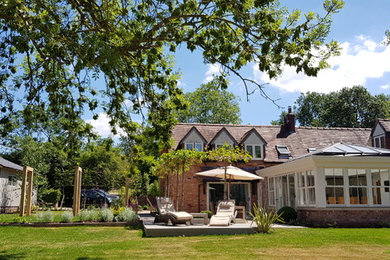 Imagen de jardín de estilo de casa de campo grande en verano en patio trasero con jardín francés, exposición total al sol y adoquines de piedra natural