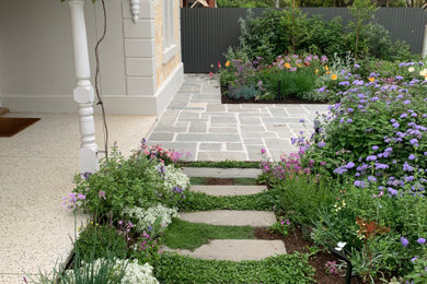 Medium sized modern front full sun garden for spring in Adelaide with a garden path, natural stone paving and a wood fence.