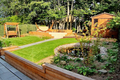 Foto de jardín nórdico de tamaño medio en verano en patio trasero con muro de contención, exposición parcial al sol y adoquines de piedra natural