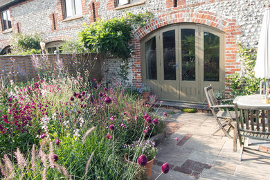 This is an example of a small farmhouse back xeriscape full sun garden for summer in Sussex with natural stone paving.