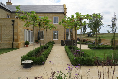 This is an example of an expansive rural back formal full sun garden for summer in West Midlands with a fire feature and natural stone paving.