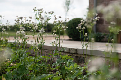 Réalisation d'un grand jardin arrière champêtre l'été avec une exposition ensoleillée et des pavés en pierre naturelle.