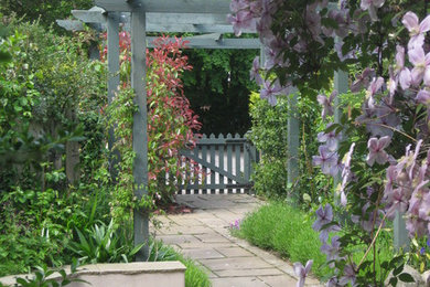 Sandstone paved path leading under a painted pergola