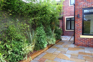 Medium sized contemporary back formal partial sun garden in London with natural stone paving.