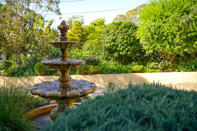 Cette image montre un jardin à la française avant traditionnel de taille moyenne avec un point d'eau, une exposition partiellement ombragée et des pavés en béton.