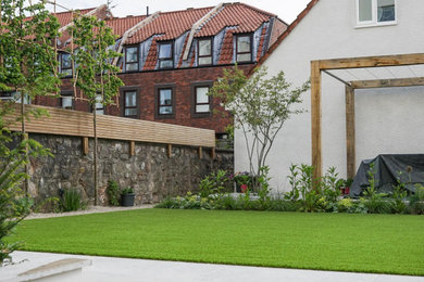Imagen de jardín actual pequeño en patio trasero con jardín francés y adoquines de piedra natural