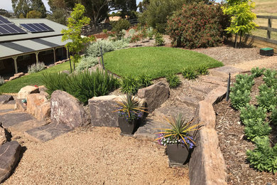 Modelo de jardín de secano actual grande en primavera en patio trasero con muro de contención, exposición total al sol y adoquines de piedra natural