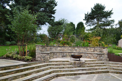 Geometrischer, Großer Klassischer Garten im Sommer, hinter dem Haus mit Feuerstelle, direkter Sonneneinstrahlung und Natursteinplatten in Manchester