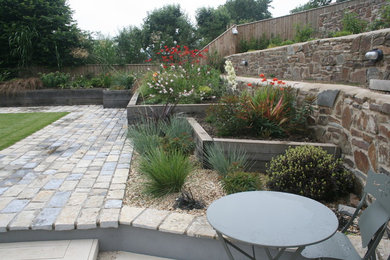 This is an example of a medium sized contemporary roof xeriscape full sun garden for summer in Devon with a retaining wall and natural stone paving.