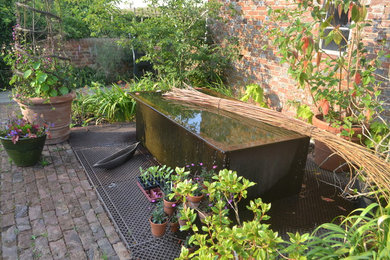 This is an example of a small country courtyard partial sun garden in Sussex with a pond.