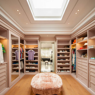 Modelo de armario vestidor unisex, actual, grande, con puertas de armario beige, suelo de madera en tonos medios y armarios con paneles empotrados