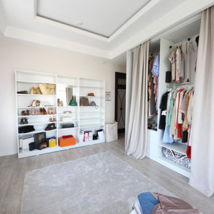 Modelo de armario vestidor de mujer, ecléctico, grande, con armarios abiertos, puertas de armario de madera clara, suelo de madera en tonos medios y suelo beige