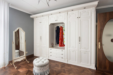 На фото: большая гардеробная комната в классическом стиле с фасадами с выступающей филенкой и темным паркетным полом