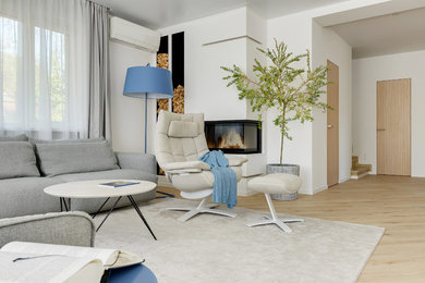 Imagen de salón abierto actual de tamaño medio con paredes blancas, suelo de madera clara, chimenea de esquina, marco de chimenea de yeso y televisor colgado en la pared