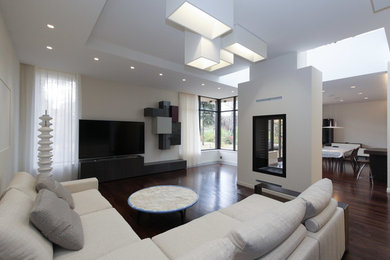 Пример оригинального дизайна: открытая гостиная комната среднего размера в современном стиле с белыми стенами, темным паркетным полом, двусторонним камином, фасадом камина из штукатурки, телевизором на стене и коричневым полом