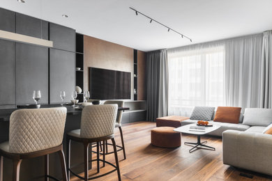 Идея дизайна: большая открытая гостиная комната в современном стиле с бежевыми стенами, паркетным полом среднего тона, телевизором на стене и коричневым полом