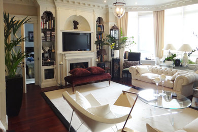 На фото: большая гостиная комната в классическом стиле с с книжными шкафами и полками, белыми стенами, темным паркетным полом, стандартным камином, фасадом камина из дерева и скрытым телевизором