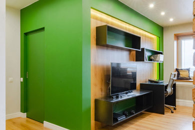 Пример оригинального дизайна: двухуровневая гостиная комната среднего размера в стиле лофт с с книжными шкафами и полками, зелеными стенами, полом из ламината, отдельно стоящим телевизором и коричневым полом без камина
