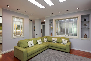 Стильный дизайн: открытая гостиная комната среднего размера в стиле фьюжн с серыми стенами, паркетным полом среднего тона, телевизором на стене и коричневым полом - последний тренд