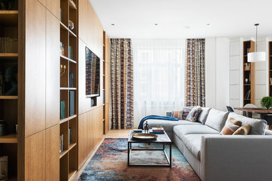Пример оригинального дизайна: открытая гостиная комната в современном стиле с с книжными шкафами и полками, белыми стенами, светлым паркетным полом, телевизором на стене и коричневым полом