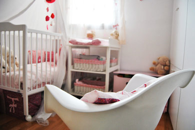 Ejemplo de habitación de bebé niña contemporánea de tamaño medio con paredes blancas y suelo de madera en tonos medios