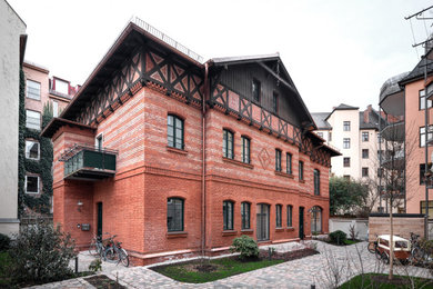 Großes, Zweistöckiges Uriges Wohnung mit Backsteinfassade, roter Fassadenfarbe, Walmdach und Blechdach in München