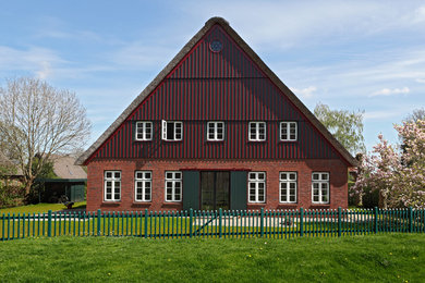 Ejemplo de fachada roja campestre extra grande de tres plantas con revestimiento de ladrillo y tejado a dos aguas