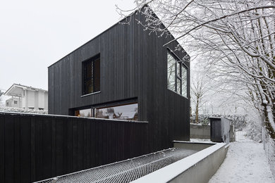 Modelo de fachada de casa negra minimalista grande de dos plantas con revestimiento de madera y tejado plano