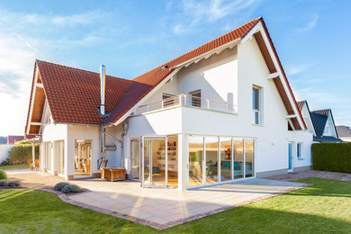 Réalisation d'une grande façade de maison blanche design en stuc à deux étages et plus avec un toit à deux pans et un toit en tuile.
