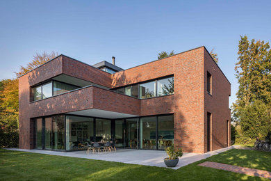 Ejemplo de fachada de casa roja minimalista grande de dos plantas con revestimiento de ladrillo y tejado plano
