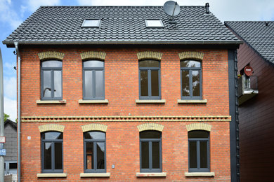Mittelgroßes, Dreistöckiges Klassisches Wohnung mit Backsteinfassade, roter Fassadenfarbe, Satteldach, Ziegeldach, blauem Dach und Verschalung in Hannover