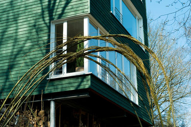 Esempio della facciata di una casa verde moderna a tre piani di medie dimensioni con rivestimento in legno e tetto piano