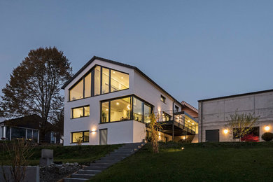 Mittelgroßes Modernes Haus mit Betonfassade, weißer Fassadenfarbe und Satteldach in München