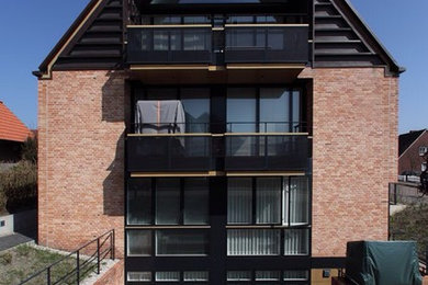 Mittelgroßes, Zweistöckiges Modernes Wohnung mit Backsteinfassade, roter Fassadenfarbe, Satteldach und Ziegeldach in Sonstige