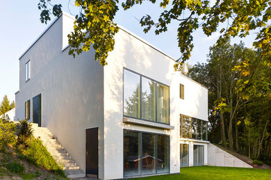 На фото: большой, трехэтажный, белый дом в современном стиле с облицовкой из цементной штукатурки и плоской крышей
