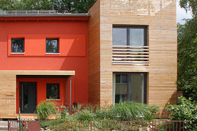 Foto della facciata di una casa rossa contemporanea a due piani con rivestimento in legno e tetto a capanna
