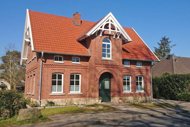 Landhausstil Einfamilienhaus mit Backsteinfassade, roter Fassadenfarbe, Satteldach, Ziegeldach und rotem Dach