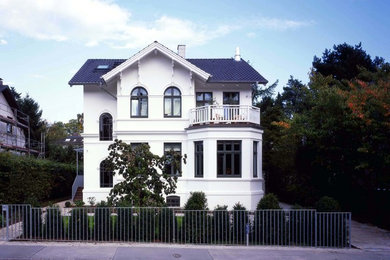 Modelo de fachada blanca de estilo de casa de campo de tamaño medio de tres plantas con tejado a dos aguas y revestimiento de estuco