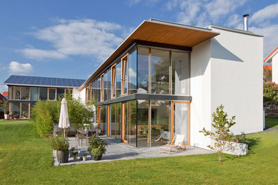 Imagen de fachada blanca actual de tamaño medio de dos plantas con revestimiento de vidrio y tejado plano