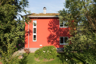 Ejemplo de fachada roja actual de dos plantas con revestimiento de piedra, tejado de un solo tendido y techo verde