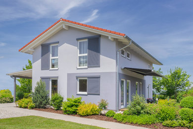 Aménagement d'une façade de maison grise classique en stuc de taille moyenne et à un étage avec un toit à deux pans et un toit en tuile.