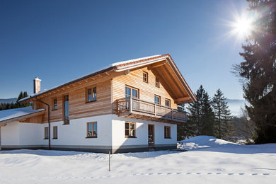 Large and white country two floor house exterior in Munich with wood cladding and a pitched roof.