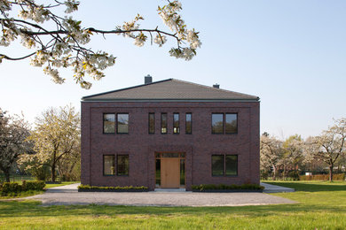 Diseño de fachada marrón campestre grande de dos plantas con revestimiento de ladrillo y tejado a cuatro aguas