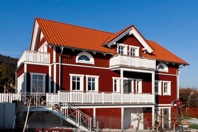 Esempio della villa rossa scandinava a due piani di medie dimensioni con rivestimento in legno, tetto a capanna e copertura in tegole