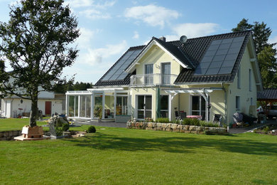 Imagen de fachada de casa amarilla clásica grande de dos plantas con revestimiento de estuco, tejado a dos aguas y tejado de teja de barro