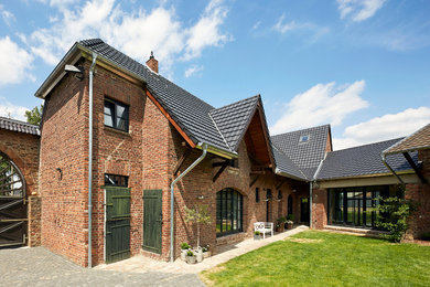 На фото: двухэтажный, кирпичный, красный, большой частный загородный дом в стиле кантри с вальмовой крышей и черепичной крышей с